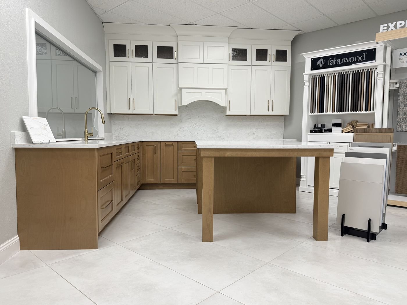 Fabuwood cabinet display showing full white upper cabinet run with glass-front doors and natural wood island in Carpet Corner Kitchen & Bath showroom, Holiday FL