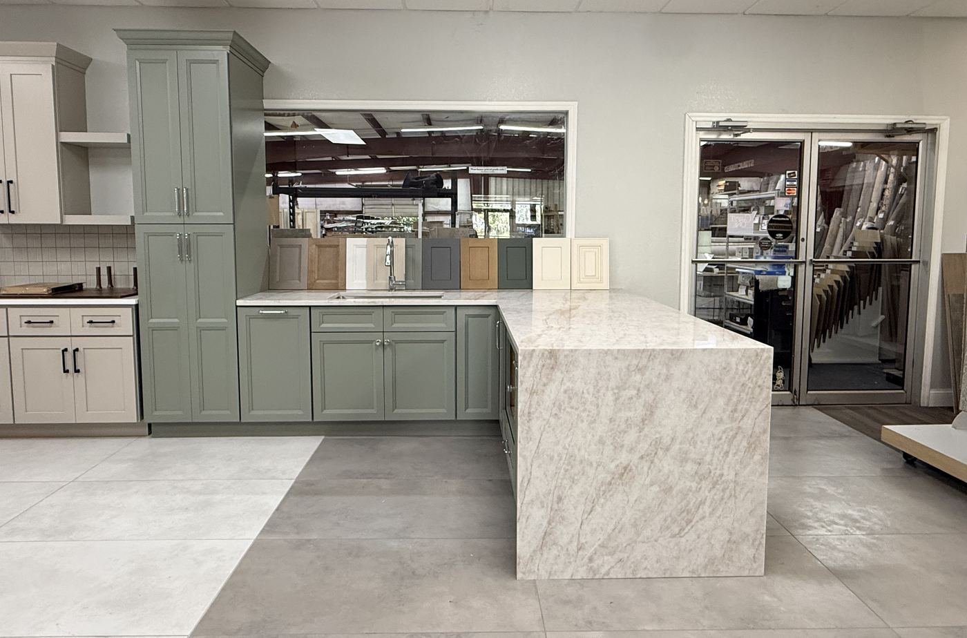 US Cabinet Depot sage green kitchen cabinets with waterfall-edge quartz island on display in Carpet Corner Kitchen & Bath showroom, Holiday FL